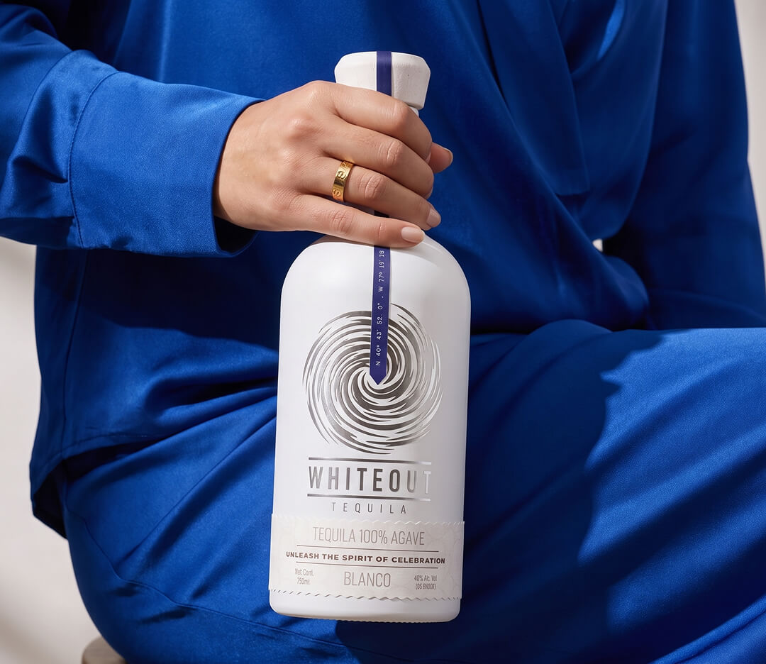 Whiteout Tequila Blanco bottle held in a bold blue lifestyle setting, highlighting premium 100% agave tequila for modern celebrations.